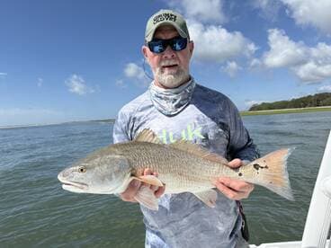 An angler proudly displaying a large Redfish while fishing in a scenic coastal environment.