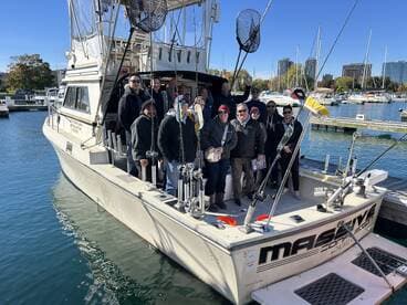 A large group of anglers gathered on the deck of the 'Mason' charter boat, ready for a day of fishing in a scenic marina setting.