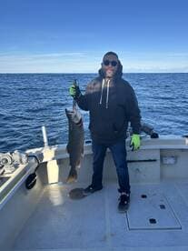 Angler proudly displaying a large Lake Trout aboard a fishing boat in open water.