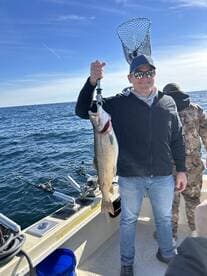 An angler proudly displaying a large Lake Trout while fishing on a boat in open waters.