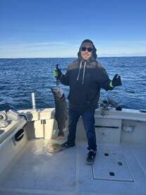 Angler proudly displaying a large Lake Trout aboard a fishing boat in open waters.