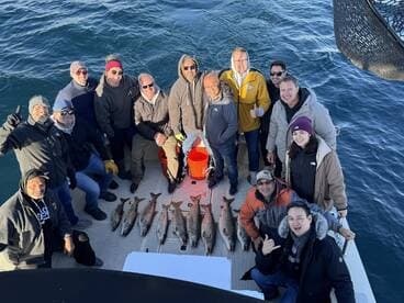 A group of anglers celebrating their successful catch of several Redfish on a fishing charter, showcasing camaraderie on the deck of the boat.