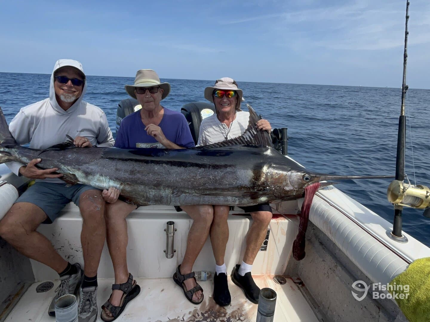 Three anglers proudly displaying a large Swordfish aboard a fishing boat in open waters.