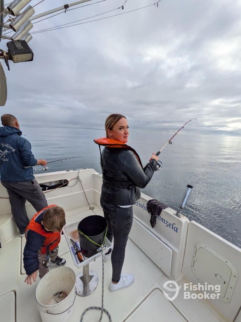 A woman fishing from a boat while a young boy explores nearby, showcasing a family fishing experience on calm waters.