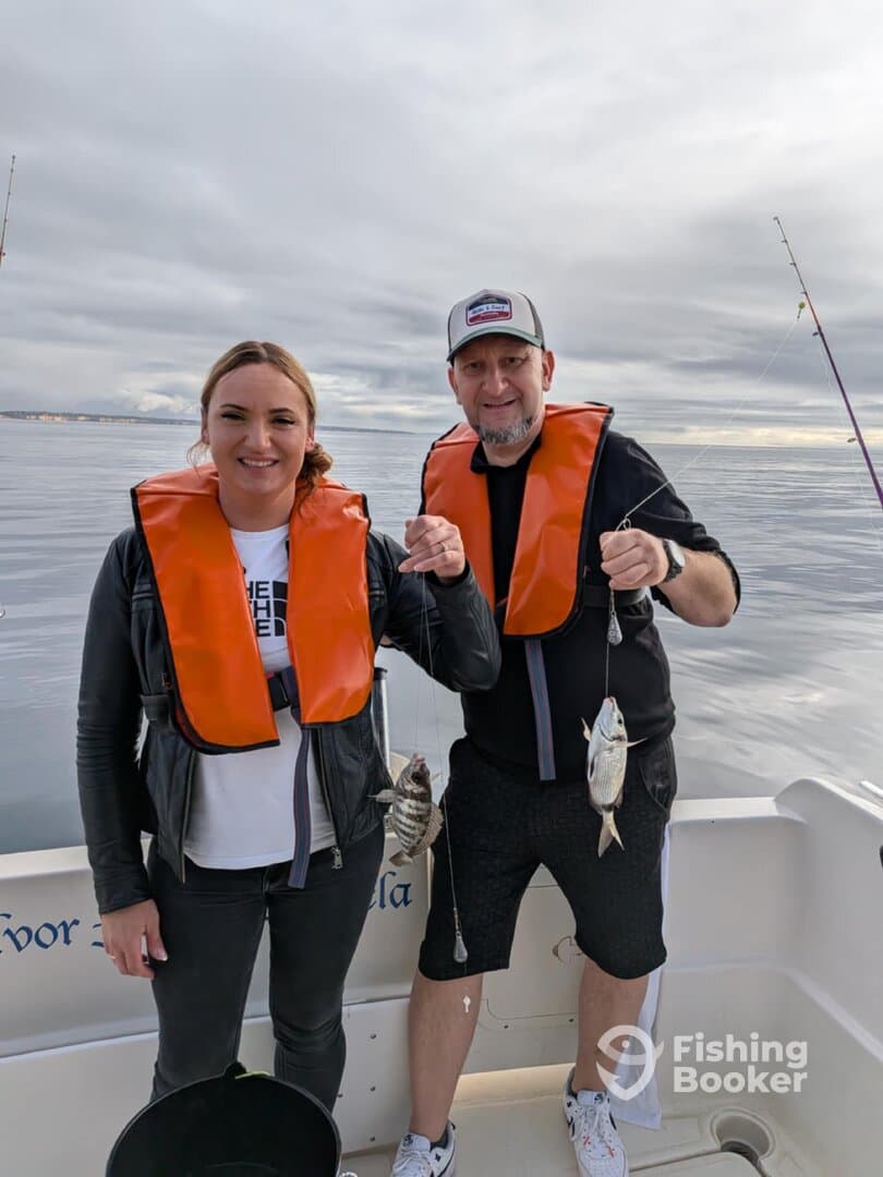 Two anglers proudly displaying their catch of Black Sea Bass while fishing on a calm day at sea.