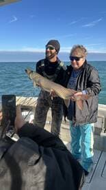 Two anglers proudly displaying a large Northern Pike on a fishing boat, enjoying a successful day on the water.
