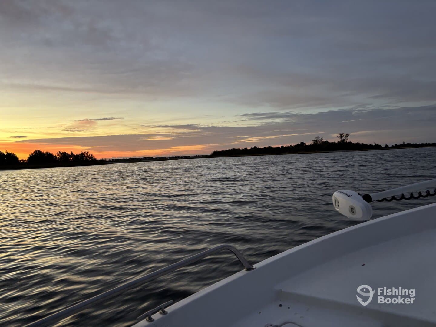 A scenic view of the boat's side during sunset, showcasing the tranquil waters and lush shoreline, perfect for a fishing adventure.