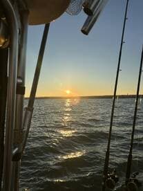 A scenic sunset view from the boat, showcasing fishing rods against the shimmering water.