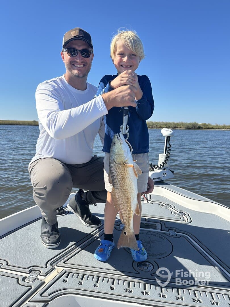 A proud young angler and his father display a large Redfish on a fishing boat, showcasing a successful day on the water.