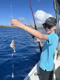 A young angler is excitedly reeling in a fish while fishing off the coast, showcasing a vibrant blue ocean backdrop.