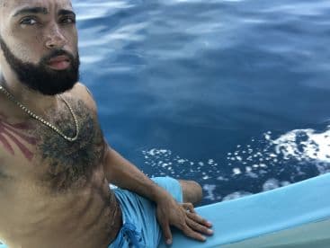 A man sitting on the side of a boat, enjoying a day out on the open water, with a clear blue ocean in the background.
