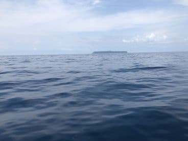 A serene view of the open ocean with a distant island visible on the horizon, capturing the tranquil fishing environment.