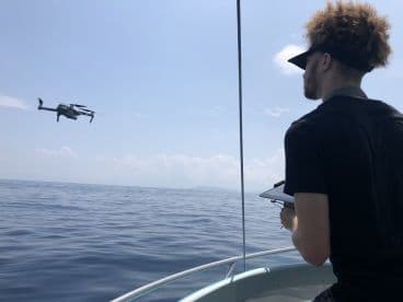 A young man operating a drone from a boat, showcasing modern fishing technology in open waters.