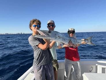 A young angler and two adults proudly displaying a large Barracuda while fishing offshore, showcasing a successful day on the water.