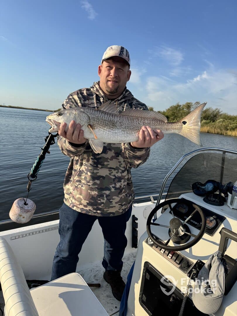 An angler proudly displaying a large Redfish while aboard a fishing boat in a serene waterway.