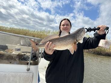 An angler proudly displaying a large Redfish while on a boat in a scenic fishing environment.
