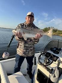 An angler proudly displaying a large Redfish while aboard a fishing boat in a serene waterway.