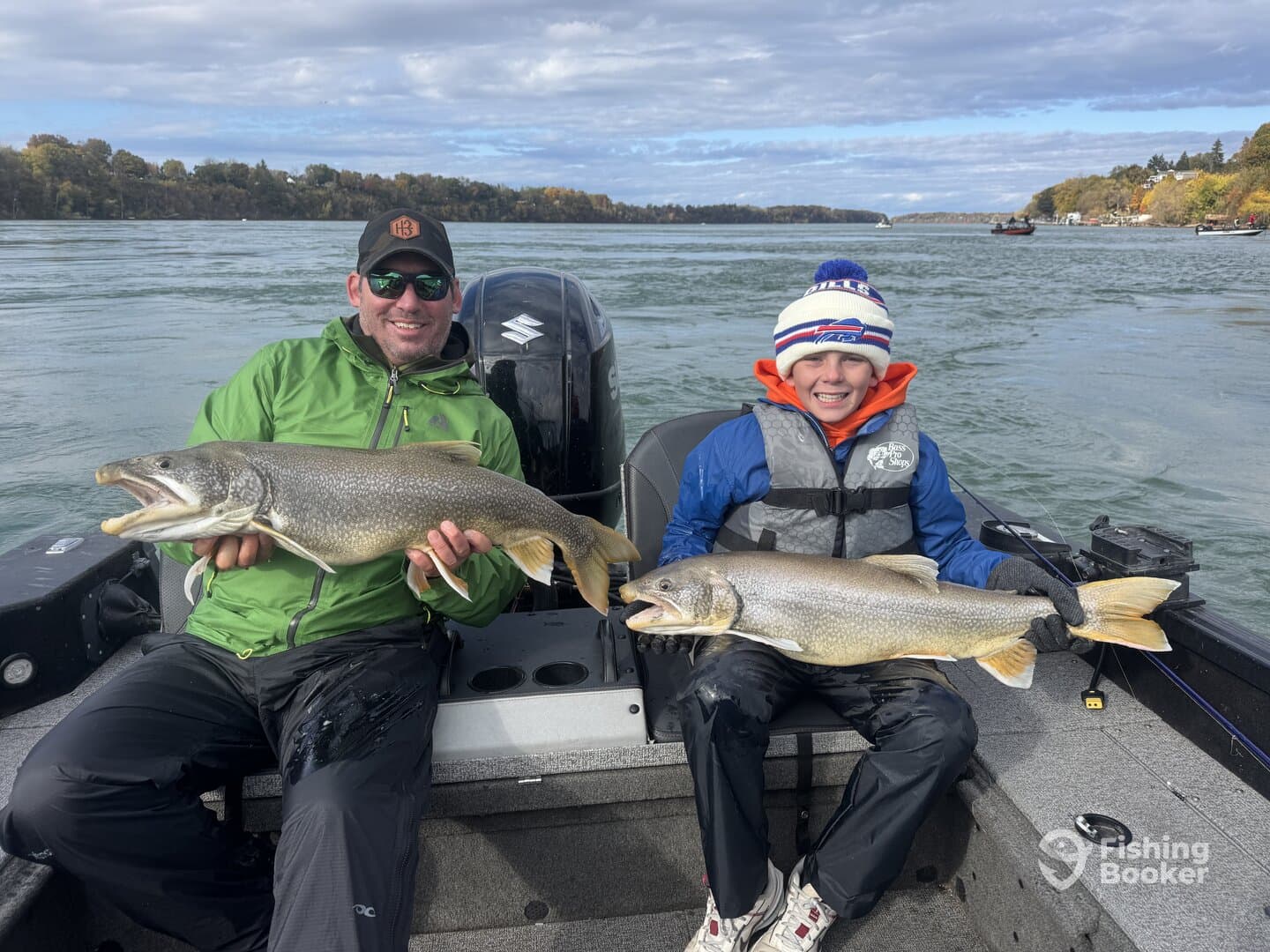 A proud father and son duo displaying their impressive catches of Lake Trout while fishing on a scenic river.