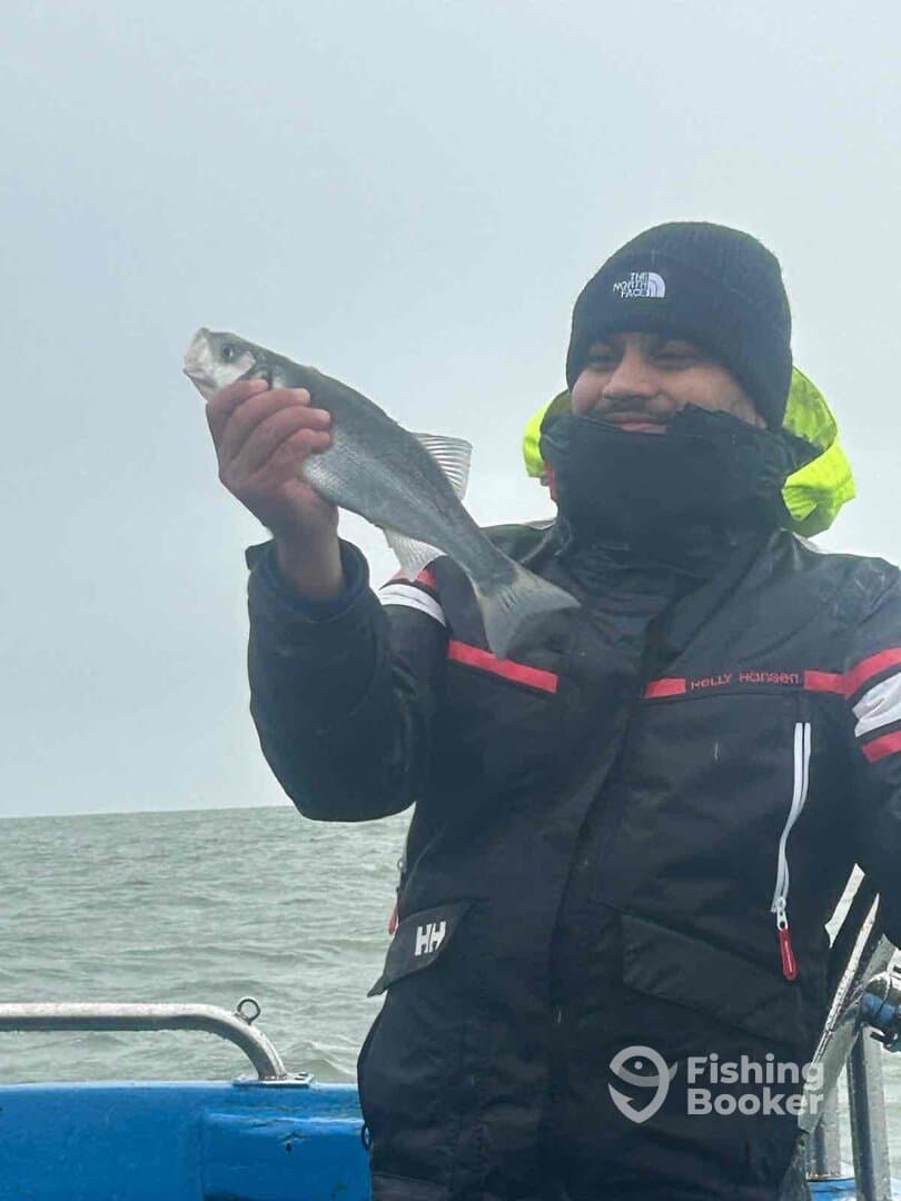 Angler proudly displaying a caught fish while aboard a boat in overcast weather.