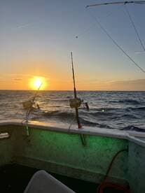 A serene sunset view from inside a fishing boat, showcasing fishing rods positioned against the backdrop of the ocean.