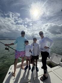 A family of four enjoying a fishing trip on a boat, with two kids holding fishing rods and a beautiful cloudy sky in the background.