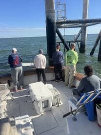 Group of anglers fishing off the side of a boat near a structure in open water, showcasing a lively fishing environment.