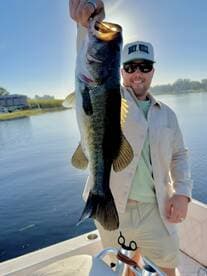Angler proudly displaying a large Largemouth Bass while fishing on a sunny day.
