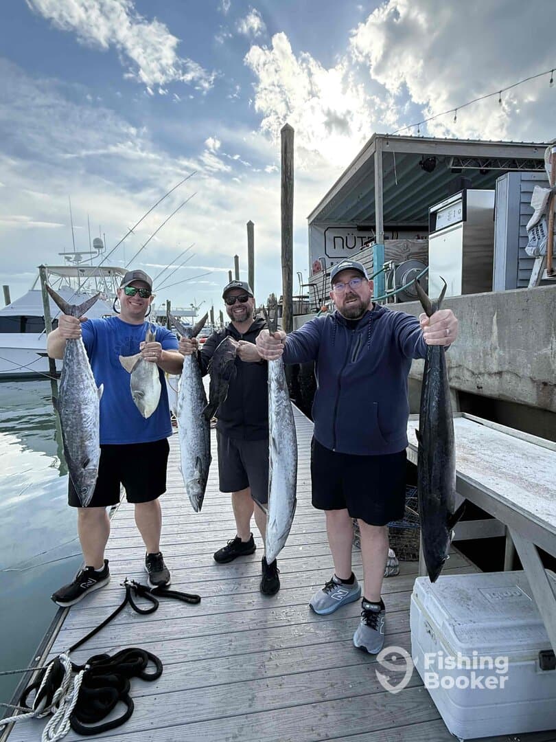 Three anglers proudly displaying their catch of Mackerel and other species at the dock after a successful fishing trip.