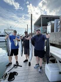 Three anglers proudly displaying their catch of Mackerel and other species at the dock after a successful fishing trip.