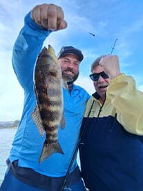 Two anglers proudly displaying a colorful Spotted Sea Trout while fishing on a sunny day.