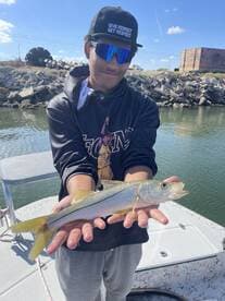 Young angler proudly displaying a Snook caught while fishing from a boat in a coastal waterway.