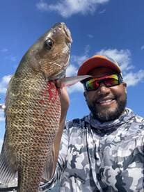 Angler proudly displaying a large Redfish against a clear blue sky while out on the water.