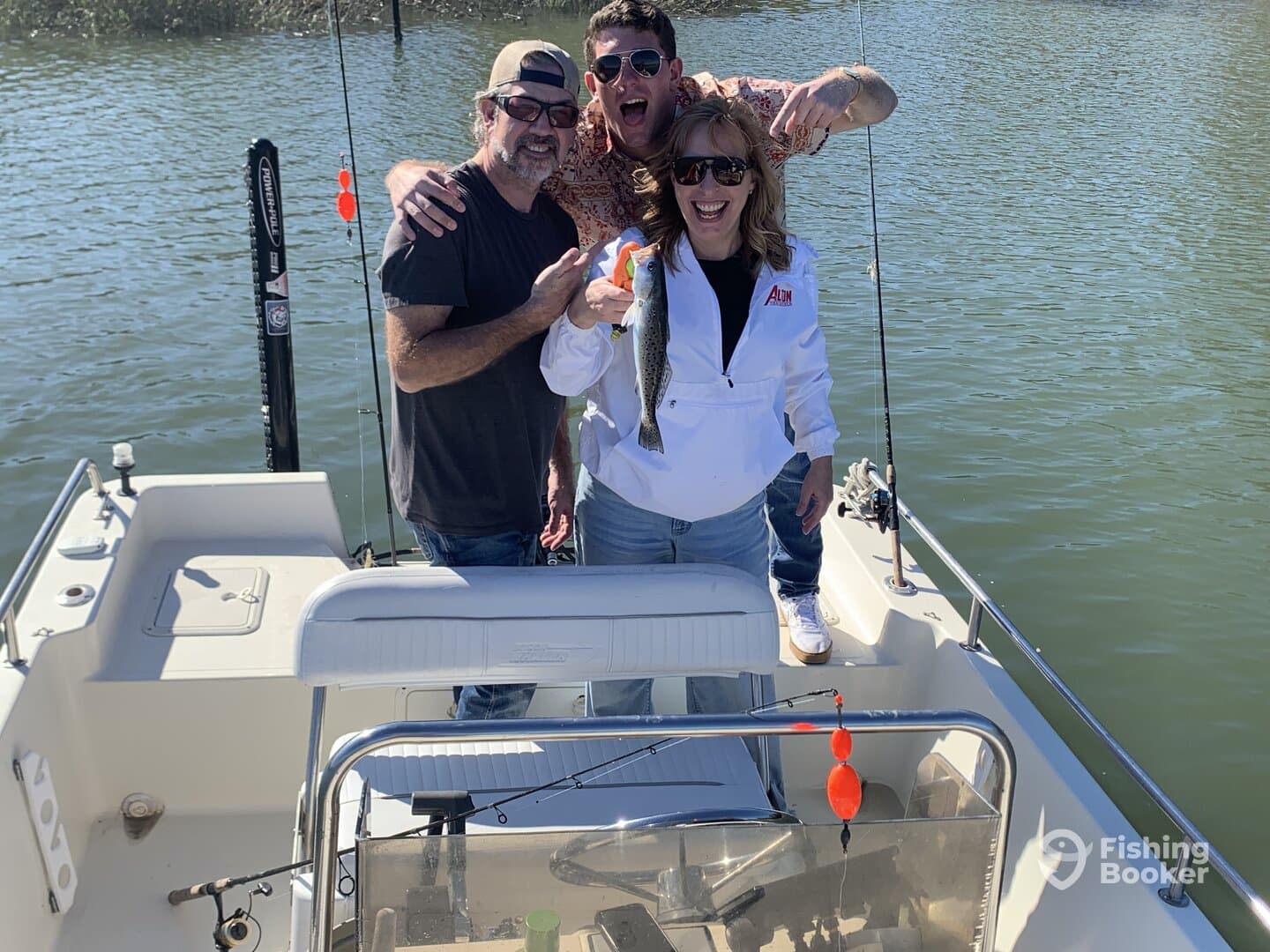 Three anglers celebrating a successful catch of a Speckled Trout while aboard a fishing boat in a scenic waterway.