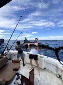 Angler proudly displaying a large Marlin aboard a sport fishing boat in open waters, showcasing a successful deep-sea fishing adventure.