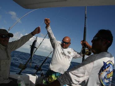 Three anglers aboard a boat celebrating the catch of a small fish while fishing in open waters.