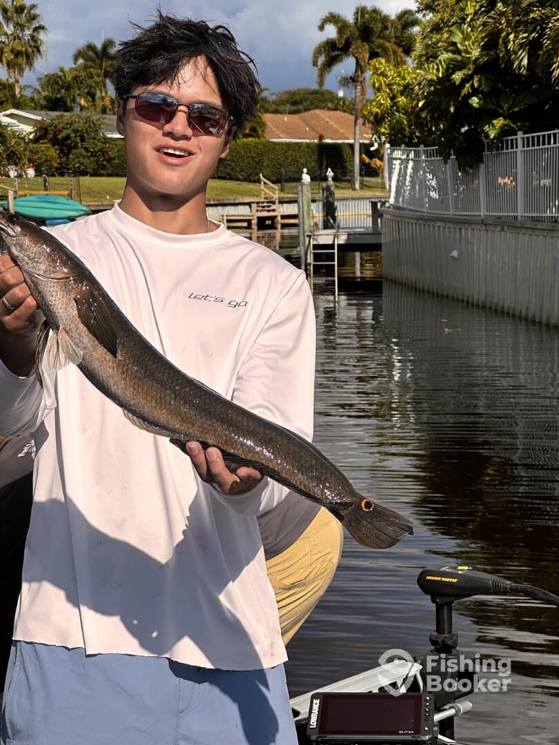 Young angler proudly displaying a large Snook while standing by the water in a residential fishing area.