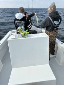 Young anglers actively fishing on a boat, with one holding a striped bass while another assists, showcasing a lively fishing experience.
