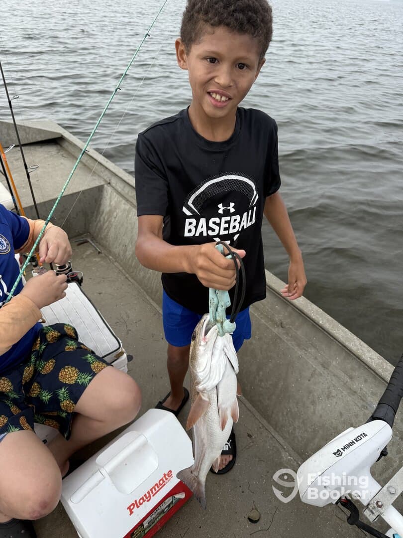A young angler proudly displaying a catch of two fish while fishing from a small boat, showcasing a fun day on the water.