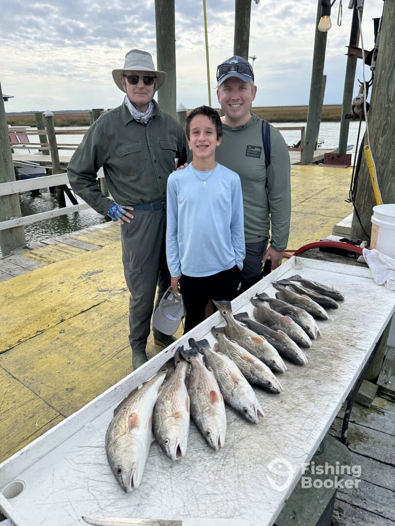 A family proudly displays their catch of Redfish on a dock after a successful fishing trip.