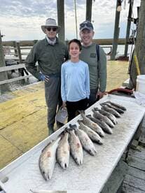 A family proudly displays their catch of Redfish on a dock after a successful fishing trip.