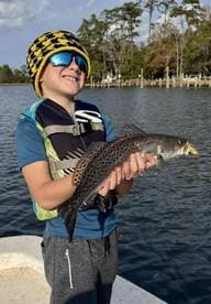 A young angler proudly displaying a Speckled Trout while fishing on a calm waterway, showcasing a fun day on the water.