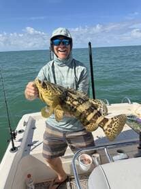 Angler proudly displaying a large Goliath Grouper while fishing on a boat in clear waters.