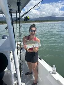 An angler proudly displaying a Silver Trevally while fishing from a boat in a scenic coastal environment.