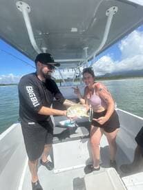 Two anglers proudly displaying a Yellowtail Snapper on a boat during a sunny fishing trip.