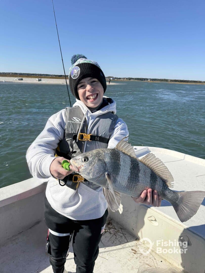 A young angler proudly displaying a Black Drum caught while fishing from a boat on a sunny day.