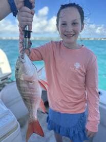 A young girl proudly displaying a Snapper caught during a fishing trip, with a vibrant blue ocean backdrop.