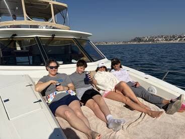 A family enjoying a relaxing day on a boat, lounging on the deck with scenic coastal views in the background.