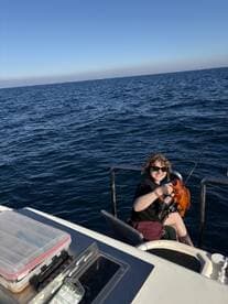 A smiling angler holding a vibrant red fish while seated on a boat, enjoying a sunny day on the water.