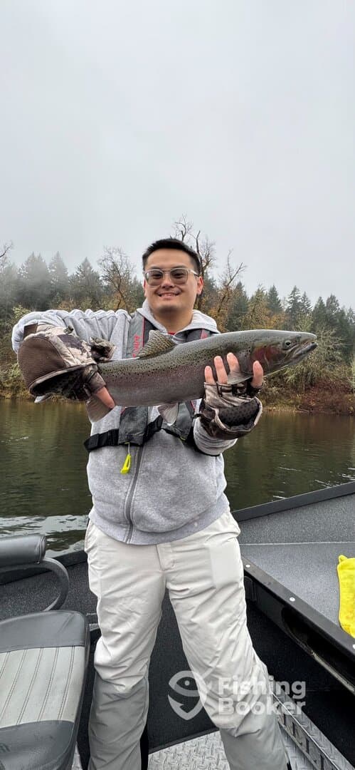Angler proudly displaying a Rainbow Trout while fishing on a river, showcasing a successful catch in a scenic environment.