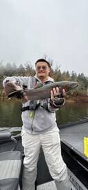 Angler proudly displaying a Rainbow Trout while fishing on a river, showcasing a successful catch in a scenic environment.